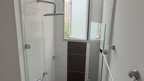 A modern bathroom with a glass shower enclosure, white tiled walls, and a window providing natural light. - Hermoso Apartamento en la mejor ubicacion by Hoost 610 (Medellín)