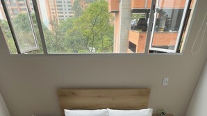A bedroom with a bed, two nightstands, a window, and a view of buildings. - Hermoso Apartamento en la mejor ubicacion by Hoost 610 (Medellín)