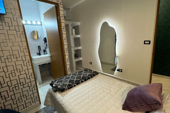 A bedroom with a bed, a bedside table, a mirror, and a wardrobe.