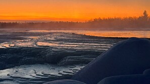 A natural landscape with a river, terraced formations, and a forest in the background. - ÁILU - Arctic Hotel Apartments (Lannavaara)