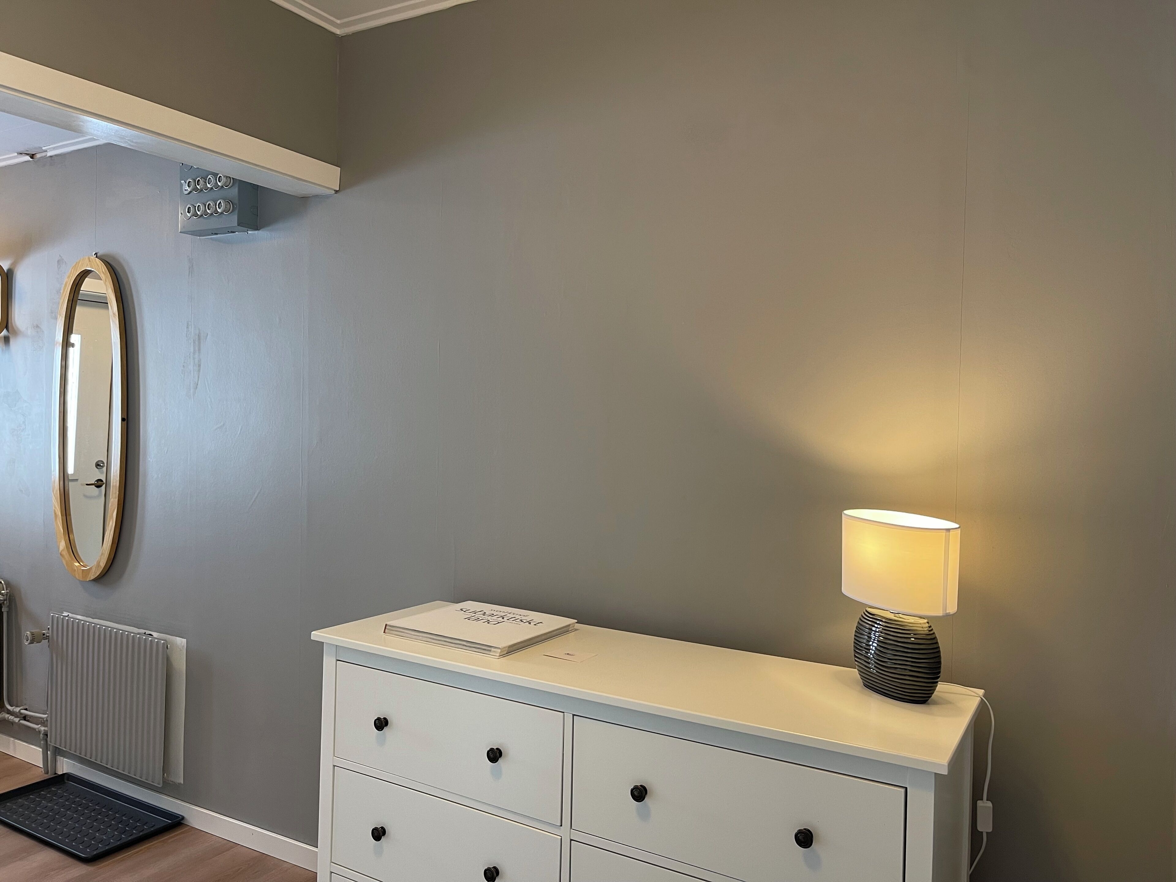 A room with a white dresser, a mirror, a radiator, and a lamp.