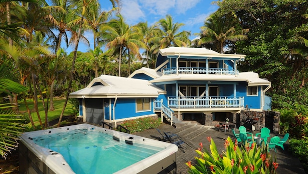 A two-story house with a balcony, a hot tub, and a patio area with chairs. - Kehena Black Sand Beach House - ocean view - swim spa (Pahoa)