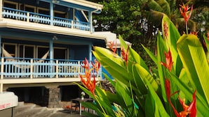 A two-story building with a blue balcony and a sign indicating a swimming area. - Kehena Black Sand Beach House - ocean view - swim spa (Pahoa)