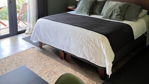 A bedroom with a bed, a nightstand, a lamp, a chair, and a view of the outdoors. - La Guarda Bed and Breakfast (Zapallar)