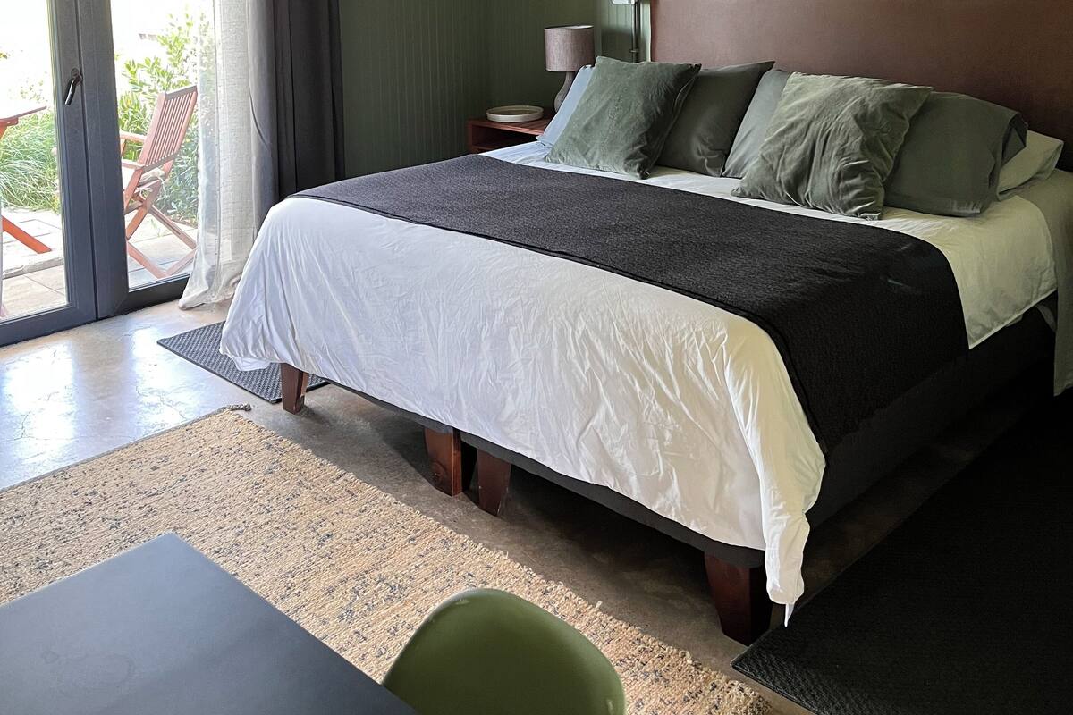 Une chambre à coucher comprenant un lit, une table de chevet, une lampe, une chaise et une vue sur l’extérieur.