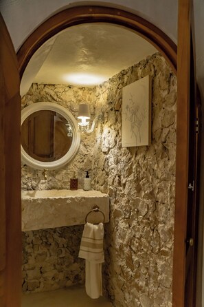A bathroom with a stone wall, a round mirror, a towel rack, and a framed drawing on the wall. - Luxury Historic 5BR Boutique hotel (Mérida)