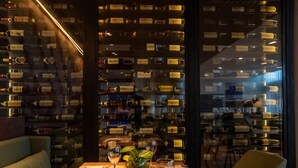 A restaurant with a wine rack wall, a table set for dining, and a view through a glass partition. - Mona Hotel (Teresina)