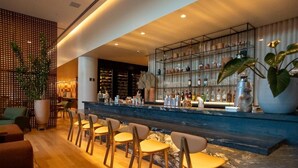 A bar area with a marble countertop, multiple seating options, and a variety of bottles and glasses on shelves. - Mona Hotel (Teresina)