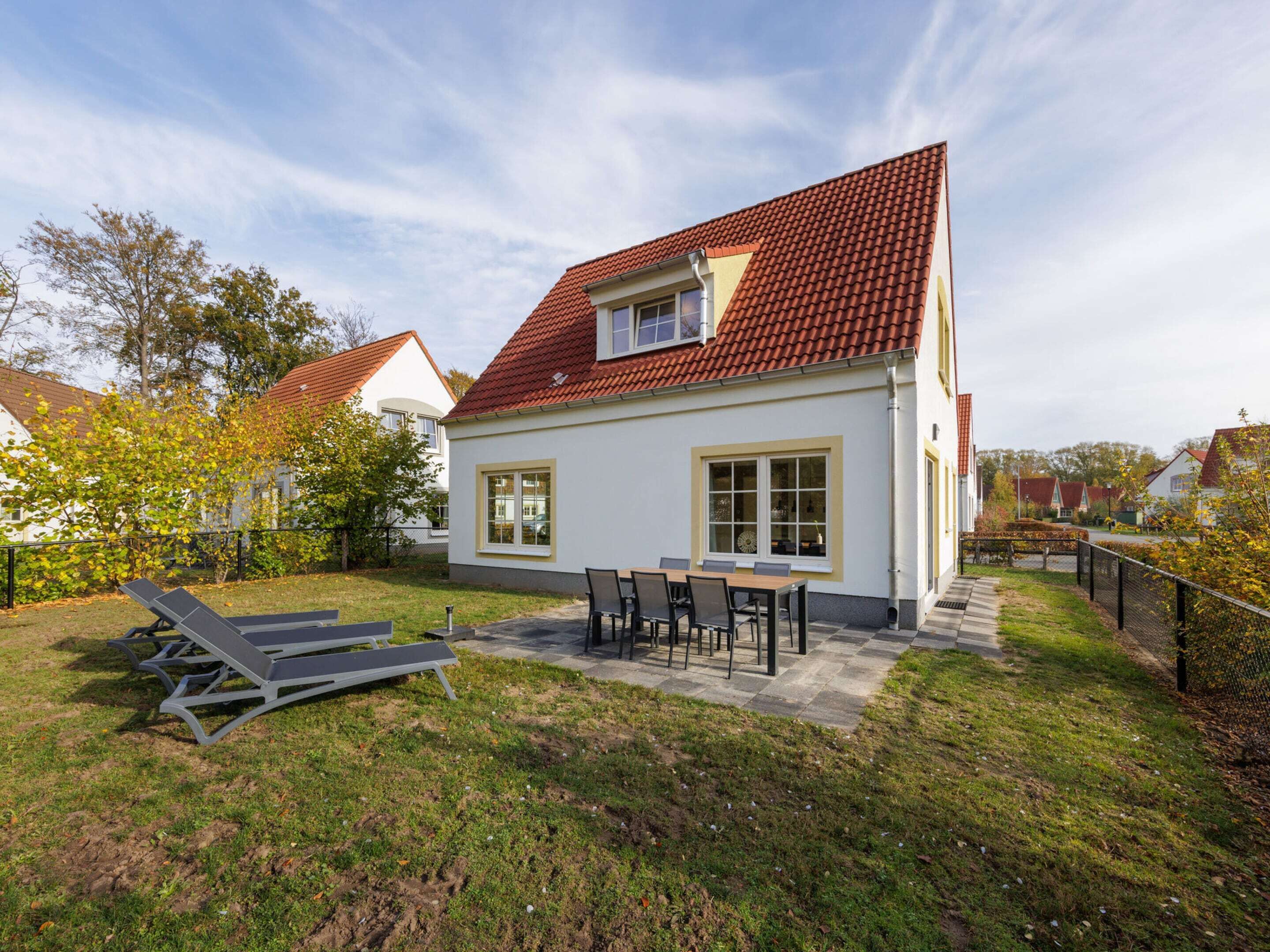 Ein zweistöckiges Haus mit rotem Ziegeldach, einer Terrasse mit Tisch und Stühlen sowie einem Rasen.