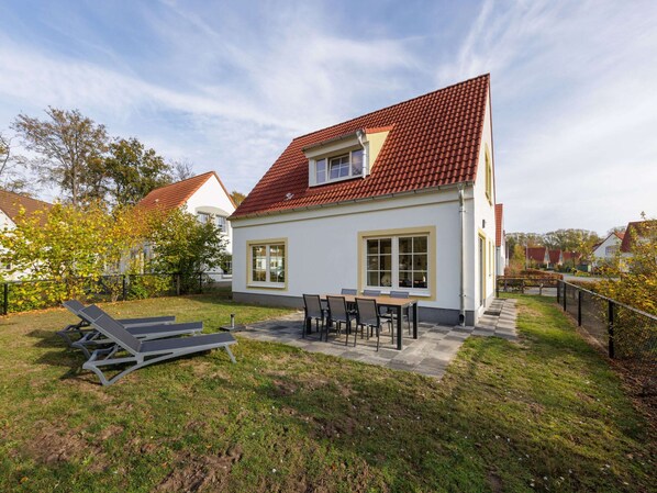 A two-story house with a red-tiled roof, a patio with a table and chairs, and a lawn. - Holiday Home in Bad Bentheim With Sauna (Bad Bentheim)