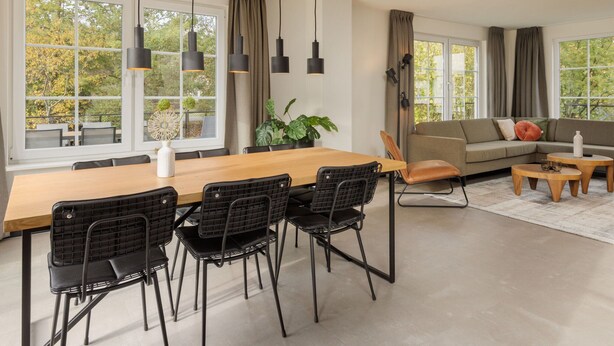 Un salon moderne avec un coin repas, de grandes fenêtres et une vue sur les arbres.