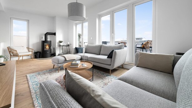 A modern living room with a fireplace, grey sofas, a wooden coffee table, and large windows offering a view of the city.