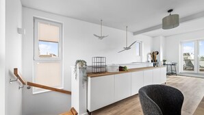 A modern kitchen with a wooden staircase, white cabinets, and a view of the outdoors.