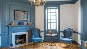 A room with a blue fireplace, two blue armchairs, a chandelier, and a large window. - Step into Colonial Charm at The Historic Powhatan Resort in Williamsburg - 2 Bd. (Williamsburg)