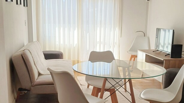 Un salon moderne avec une table à manger en verre, des chaises blanches, un canapé et un luminaire suspendu au plafond.