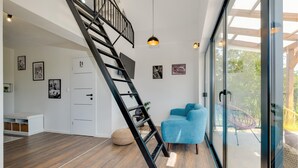 Een modern interieur met een houten vloer, een blauwe bank, een trap en een glazen deur naar buiten.