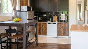 Een moderne keuken met een eethoek, houten kasten, een magnetron en uitzicht op groen.