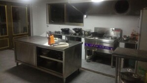 A commercial kitchen with stainless steel appliances, a large island with a sink, and overhead lighting. - Damingshan Juxianlou Homestay (Hangzhou)