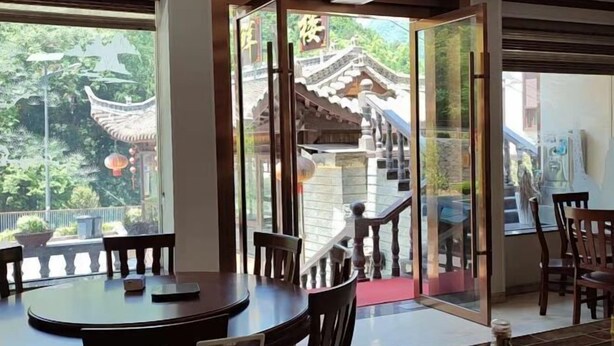 A dining area with a round table and chairs, large windows with a view of traditional architecture, and a staircase leading to an upper level. - Damingshan Juxianlou Homestay (Hangzhou)