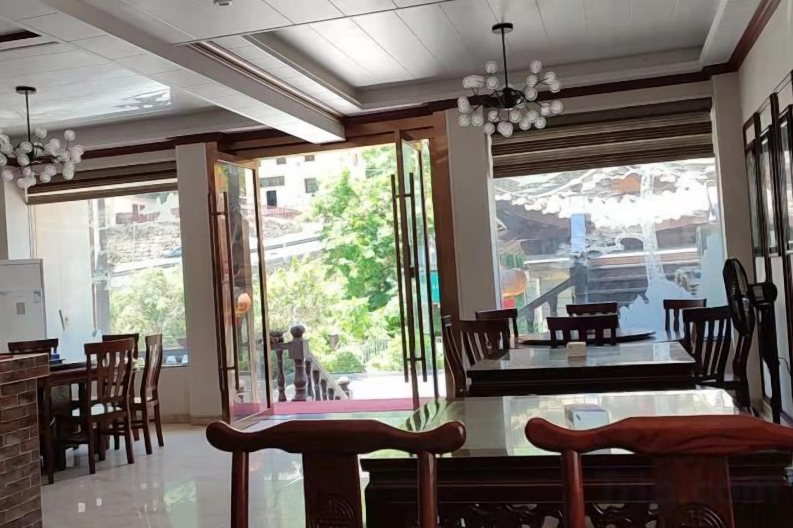 Comedor con separador de vidrio, sillas de madera y vista a un edificio y follaje exterior.