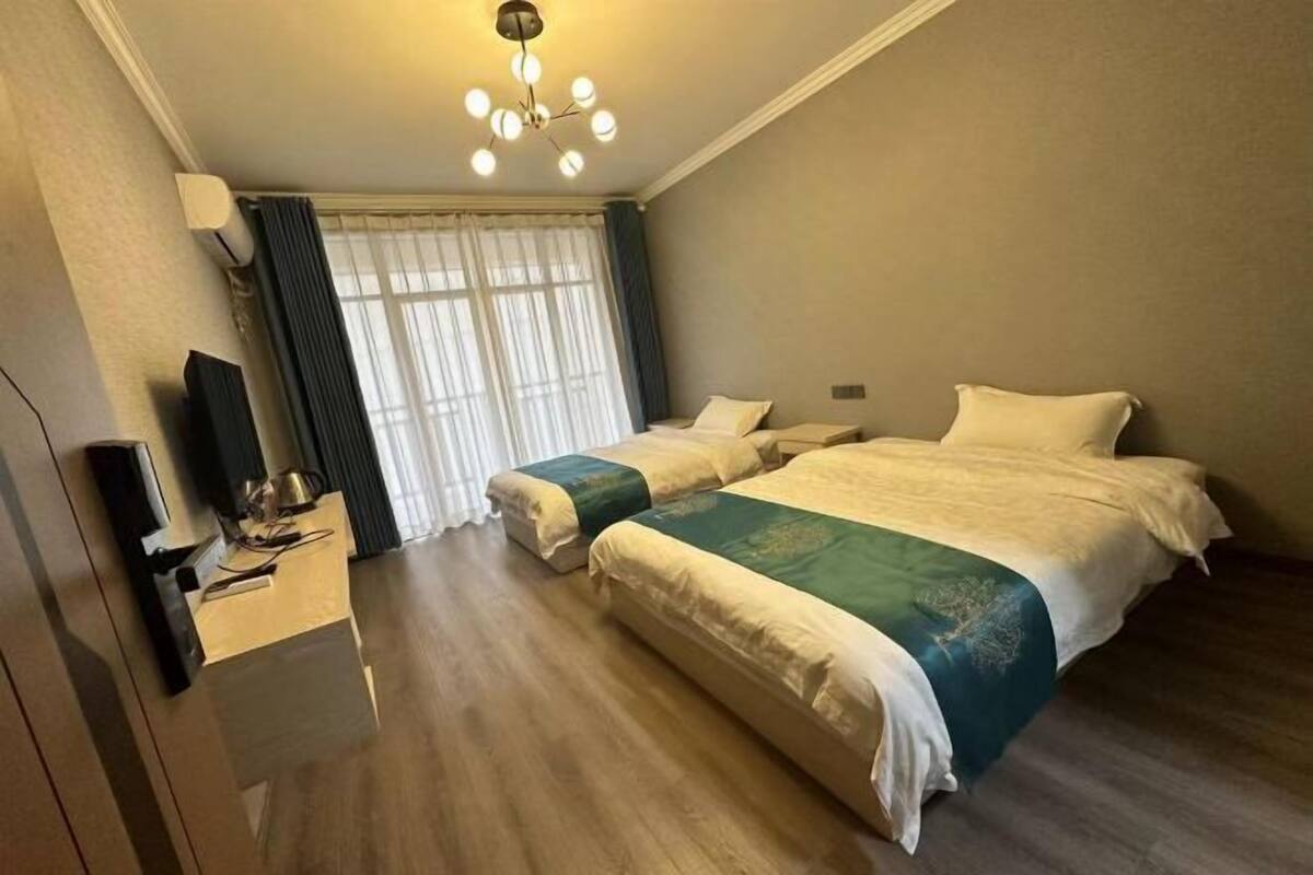 A hotel room with two beds, a desk with a computer, and a large window with curtains.