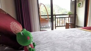 A bedroom with a bed, a green plush toy, a red pillow, and a view of a balcony with a wicker basket. - Damingshan Juxianlou Homestay (Hangzhou)