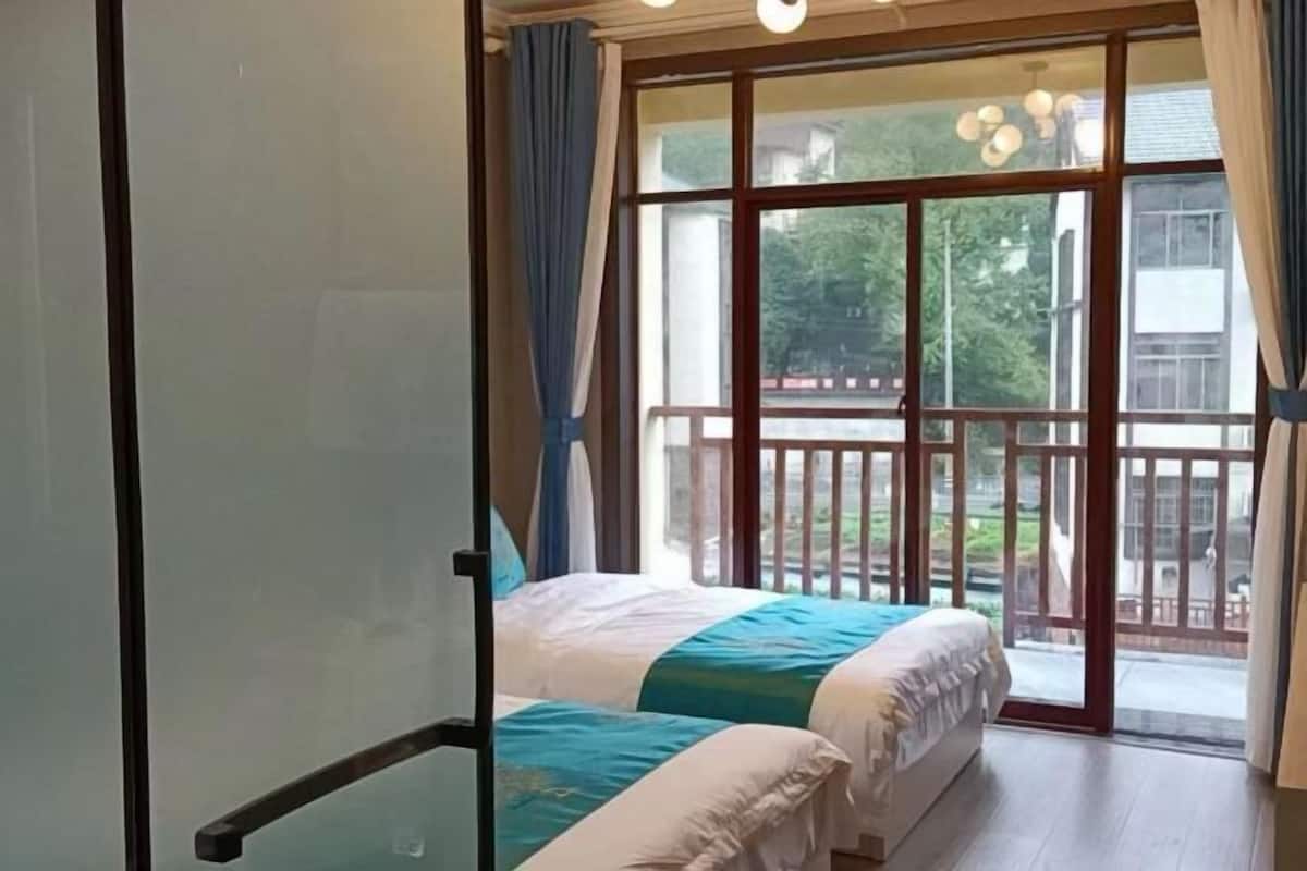 A room with two beds, a balcony with a railing, and a view of the outdoors.