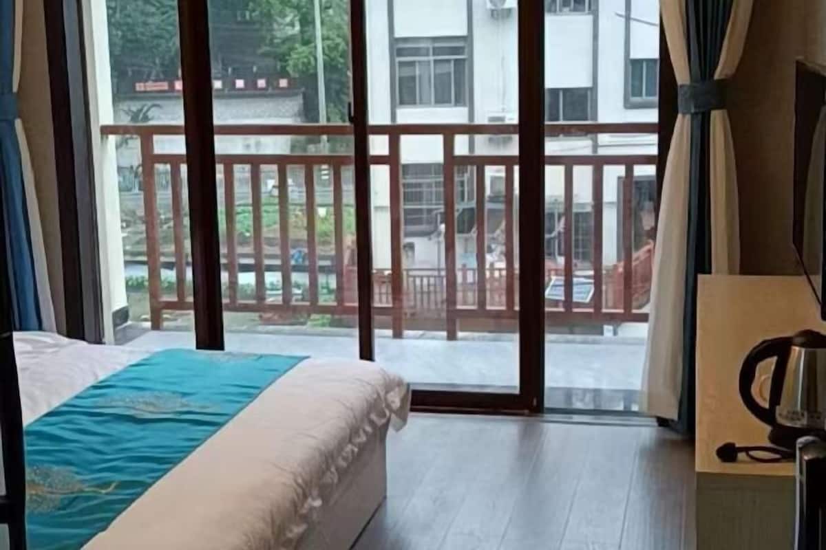 A hotel room with a bed, a view of the outside balcony, and a kettle on the table.