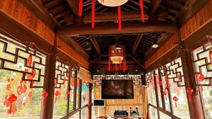 A traditional wooden interior with a TV screen, wooden beams, and red decorations. - Damingshan Juxianlou Homestay (Hangzhou)