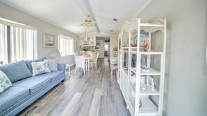 A spacious living area with a blue sofa, white chairs, and a white shelving unit with decorative items.