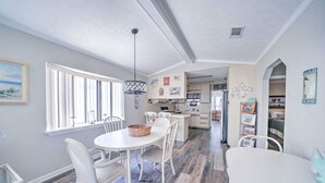A spacious kitchen with white cabinetry, a dining area with a round table and chairs, and a large window providing natural light.