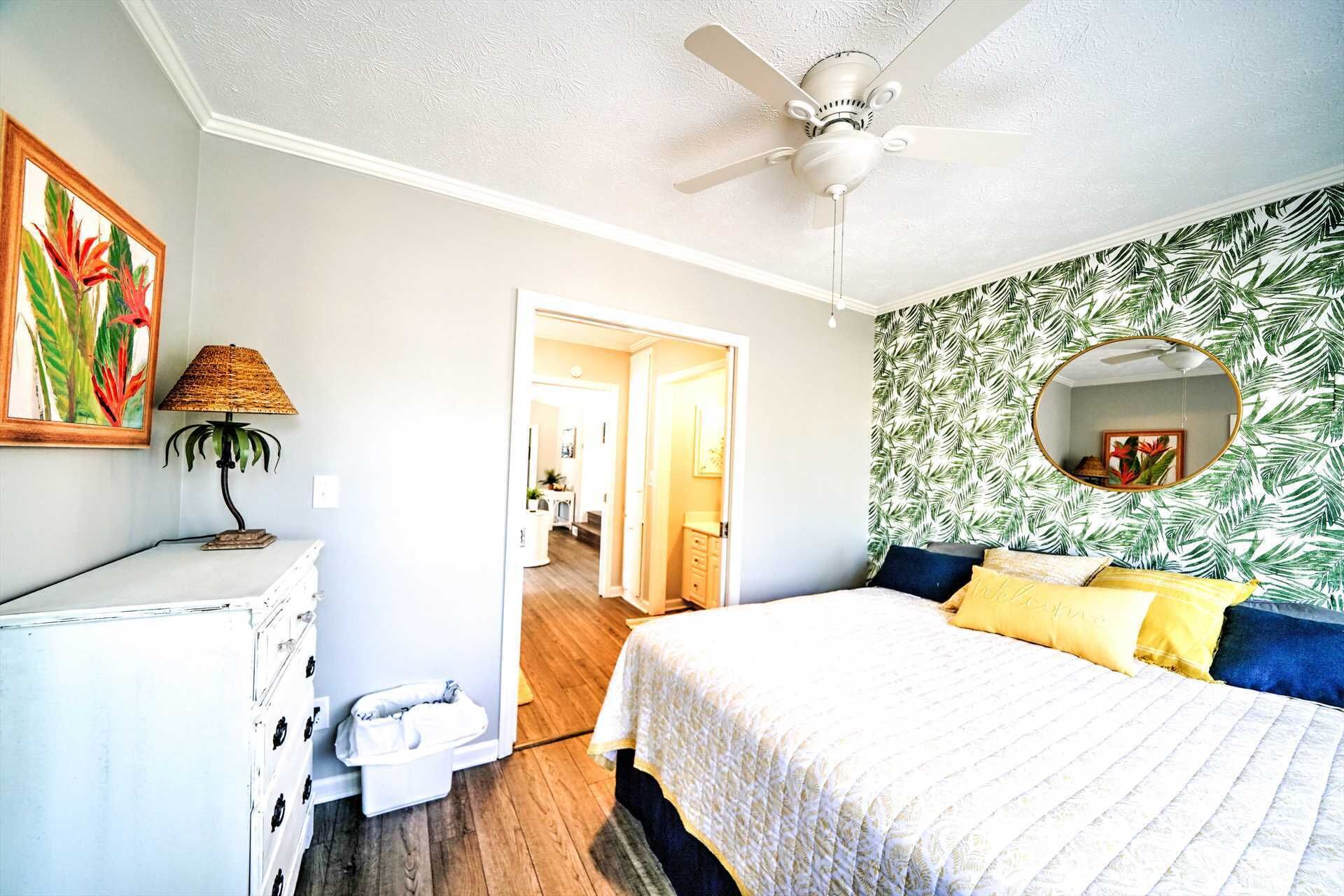 A bedroom with a bed, a ceiling fan, a dresser, a mirror, and a door leading to another room.