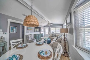 Un espace repas avec une table ronde, des chaises blanches et un luminaire suspendu en fibres tressées.