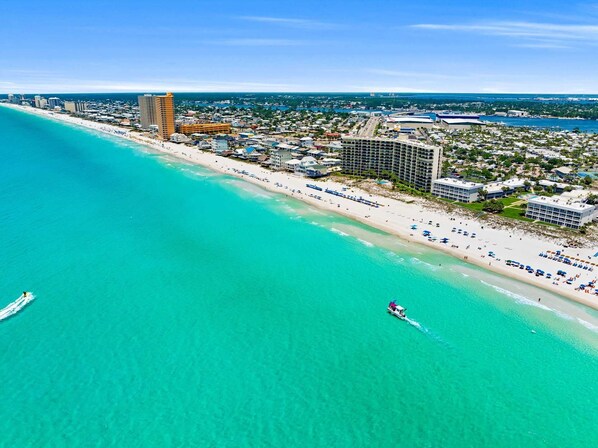 An aerial view of a coastal resort with beachfront properties, a marina, and a clear blue sky.