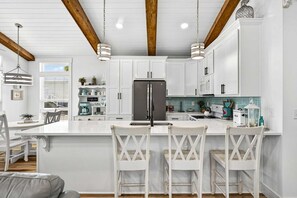 A modern kitchen with white cabinetry, a central island with bar stools, a stainless steel refrigerator, and pendant lighting.