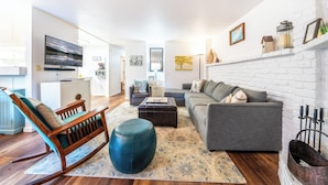 Un salon moderne avec un canapé gris, un fauteuil à bascule en bois et un pouf bleu.