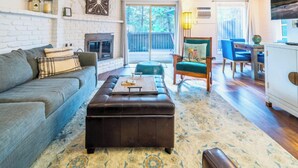 Un salon avec une cheminée, un canapé, une table basse, un fauteuil à bascule et un coin repas comprenant des chaises et une table.