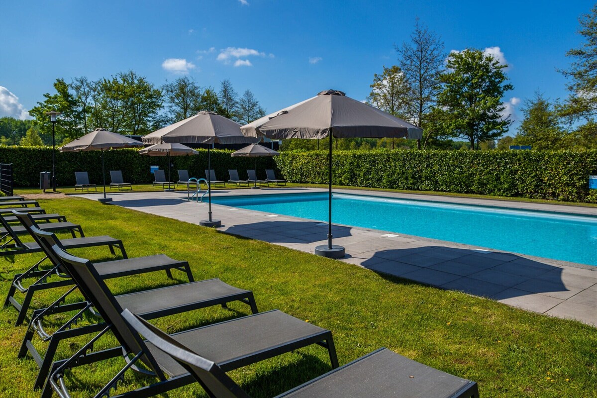Una piscina con sillas de descanso y sombrillas, rodeada de setos y árboles.