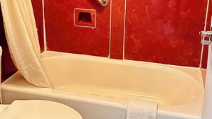 A bathroom with a red tiled wall, a white bathtub, a white toilet, and a shower with a beige curtain. - Dreamland Inn and Suites (Senatobia)