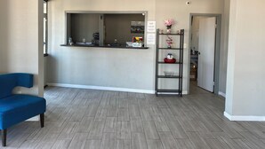 A reception area with a counter, a blue chair, a shelf with decorative items, and a door leading to another room. - Dreamland Inn and Suites (Senatobia)