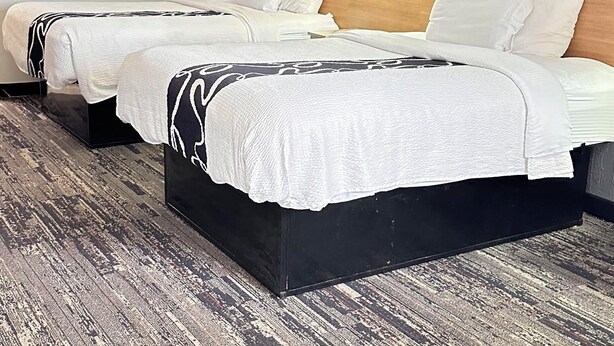 A hotel room with two beds, a wooden headboard, a large painting of a sunset pier, and a textured carpet. - Dreamland Inn and Suites (Senatobia)