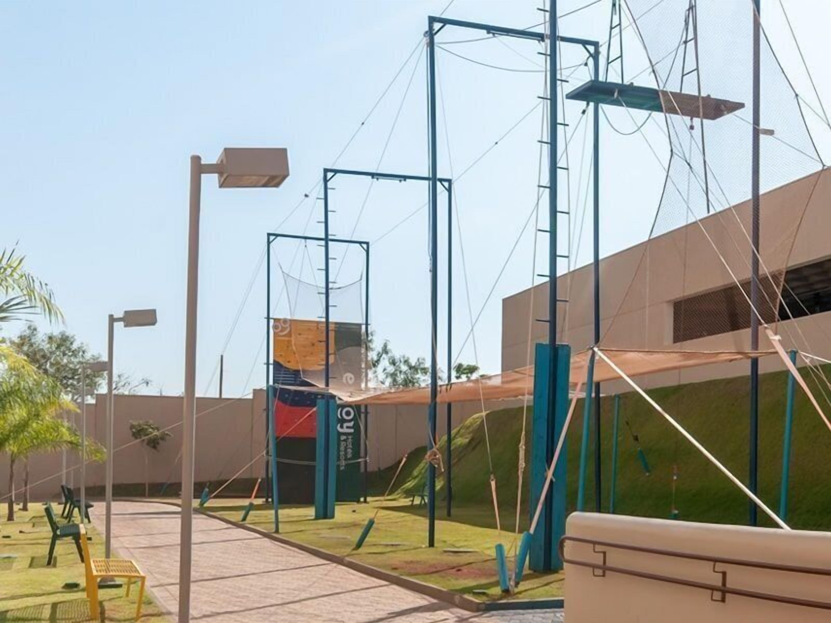 An outdoor area with a climbing wall, a basketball court, and a building in the background.