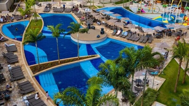 Une grande piscine extérieure divisée en plusieurs zones, entourée de chaises longues et de palmiers.