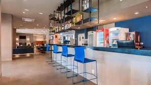 Un espace bar moderne avec des chaises bleues, un comptoir et une cuisine en arrière-plan.