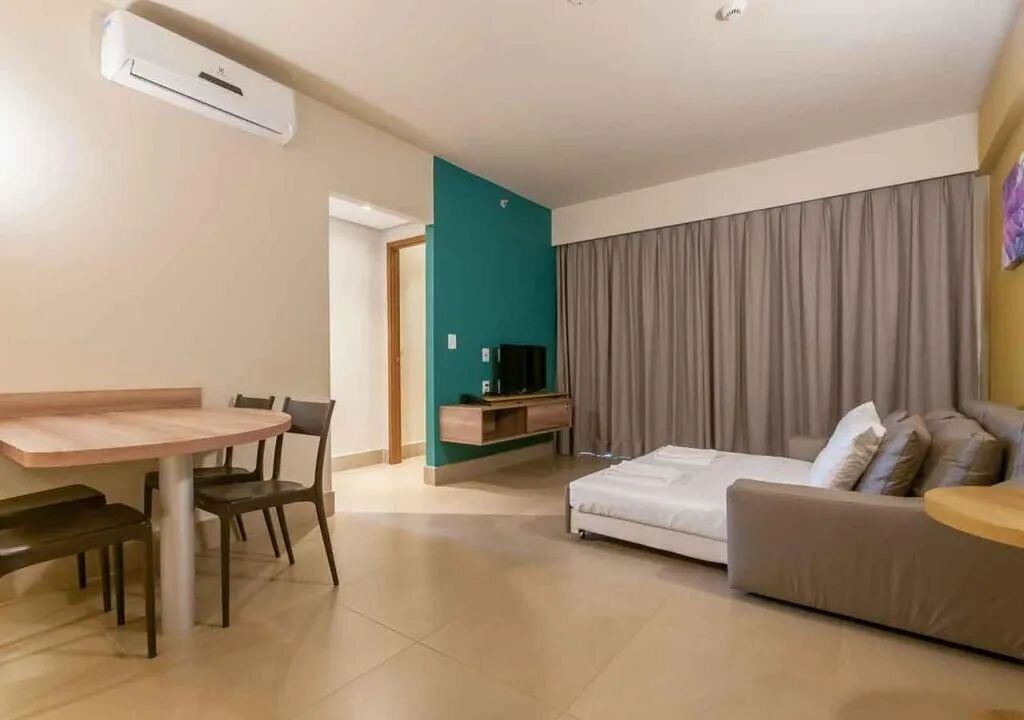 A modern living room with a sofa, a dining table with chairs, a TV on a stand, and a large window with curtains.