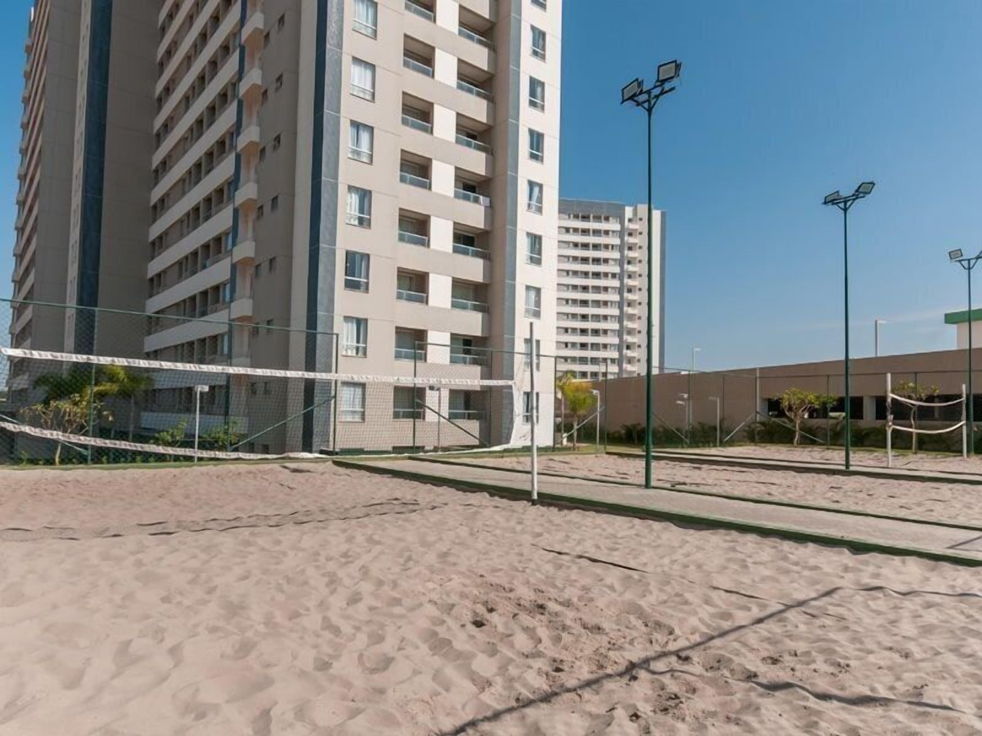 A sandy beach area with volleyball net, surrounded by tall buildings.