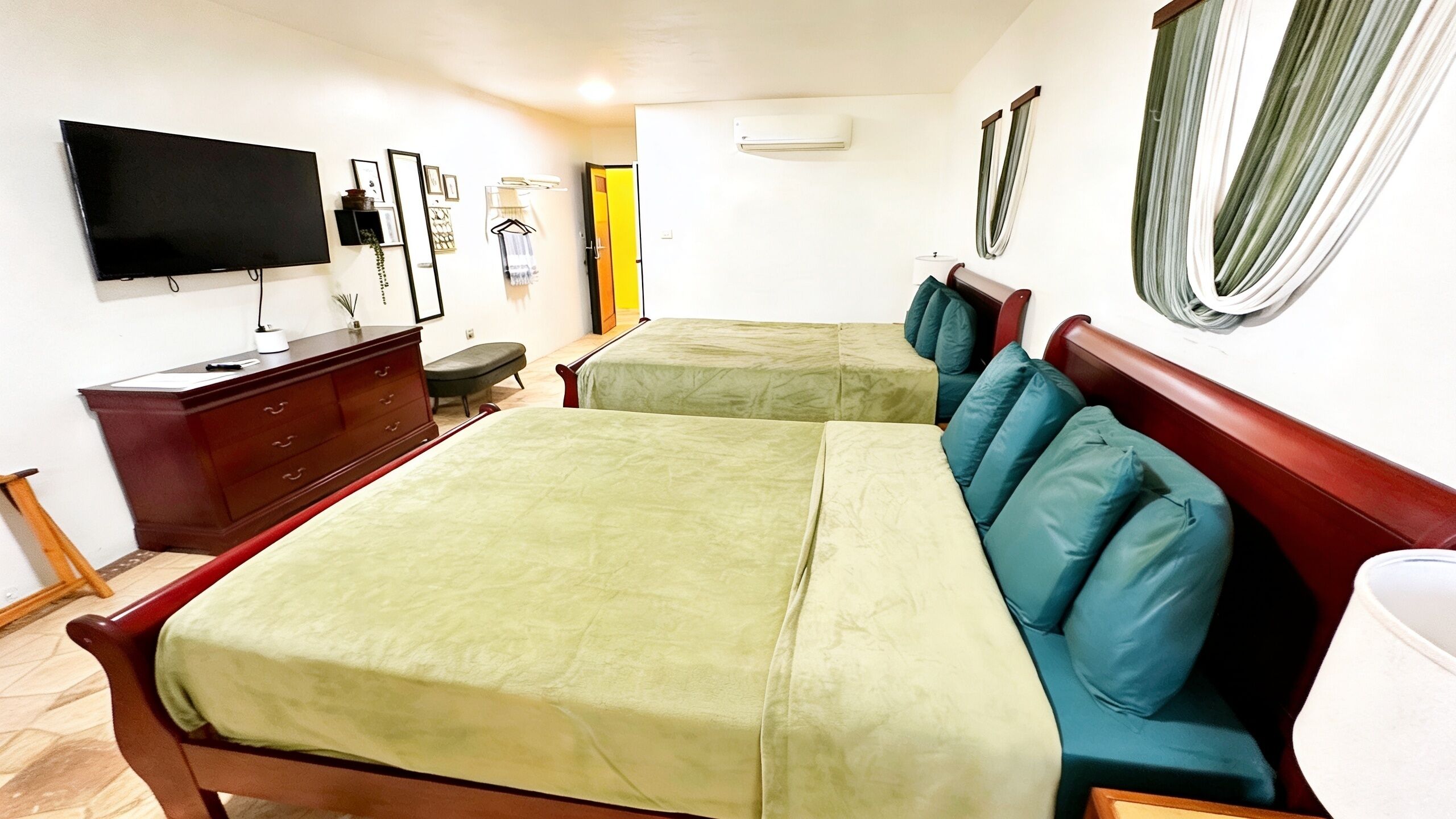 A hotel room with two beds, a TV, a dresser, and a window with curtains.