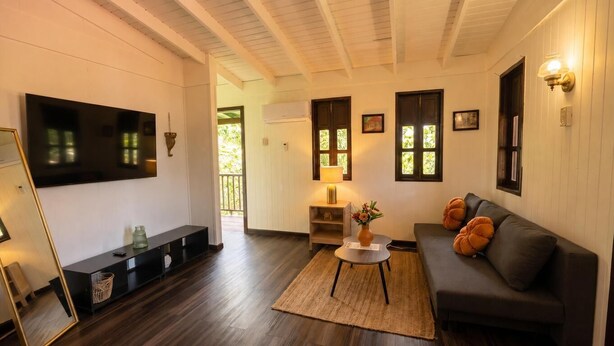 A living room with a dark sofa, a coffee table, a TV mounted on the wall, and a wooden ceiling. - El Oasis Hotel (Aguada)