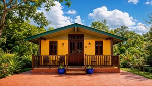 A yellow building with a green roof, a wooden porch with chairs, and a number '21' on the door. - El Oasis Hotel (Aguada)