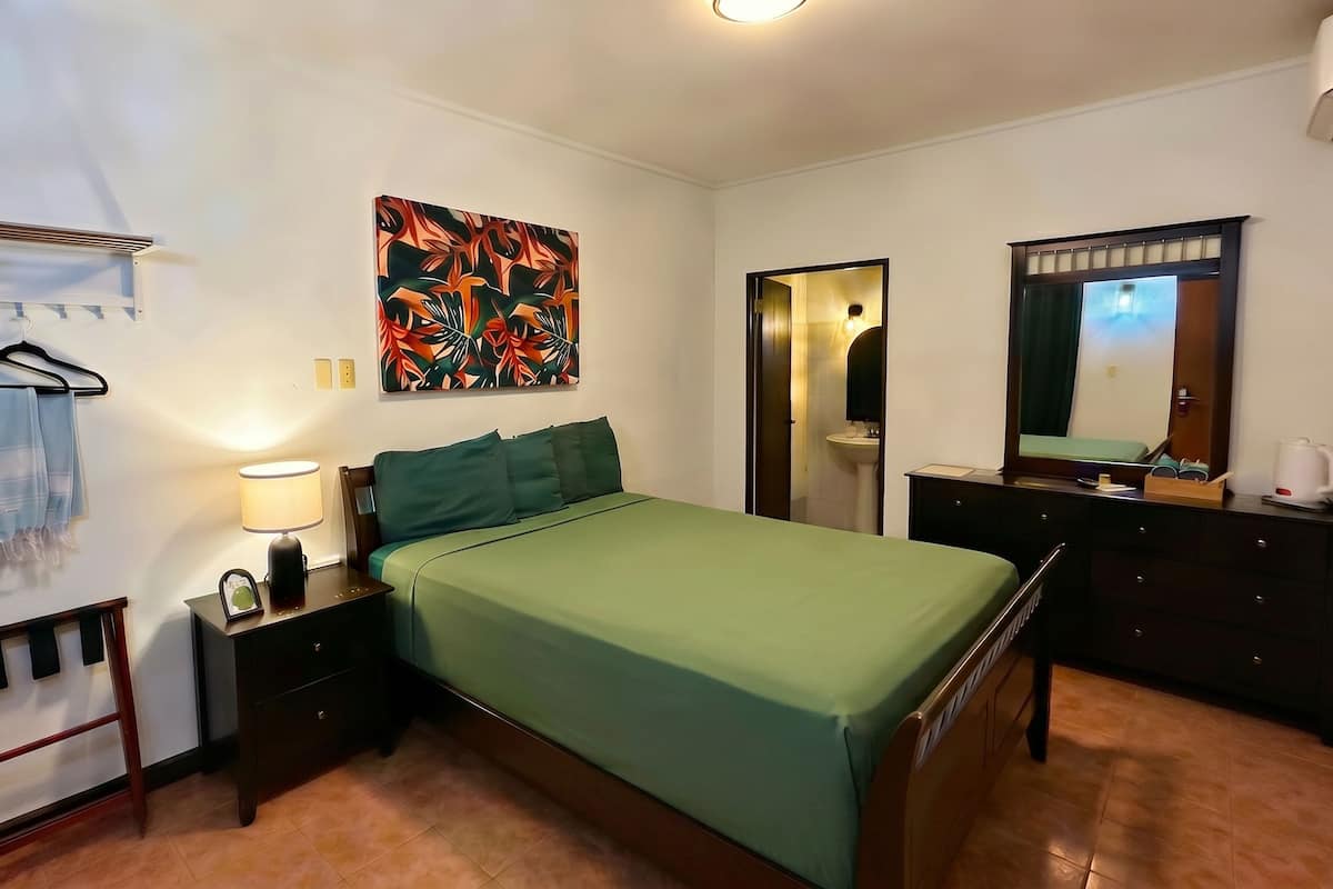 A bedroom with a bed, nightstand, lamp, and a painting on the wall.